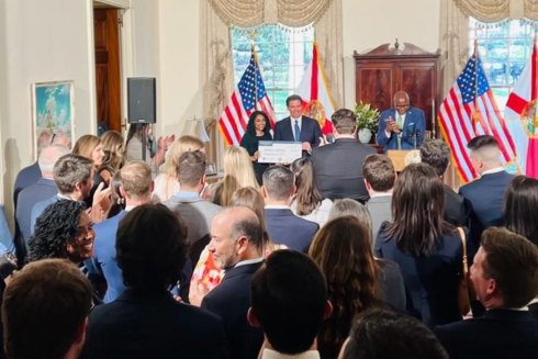 Keerthana Kallarackal receives an award in a crowded government room from Governor Ron Desantis