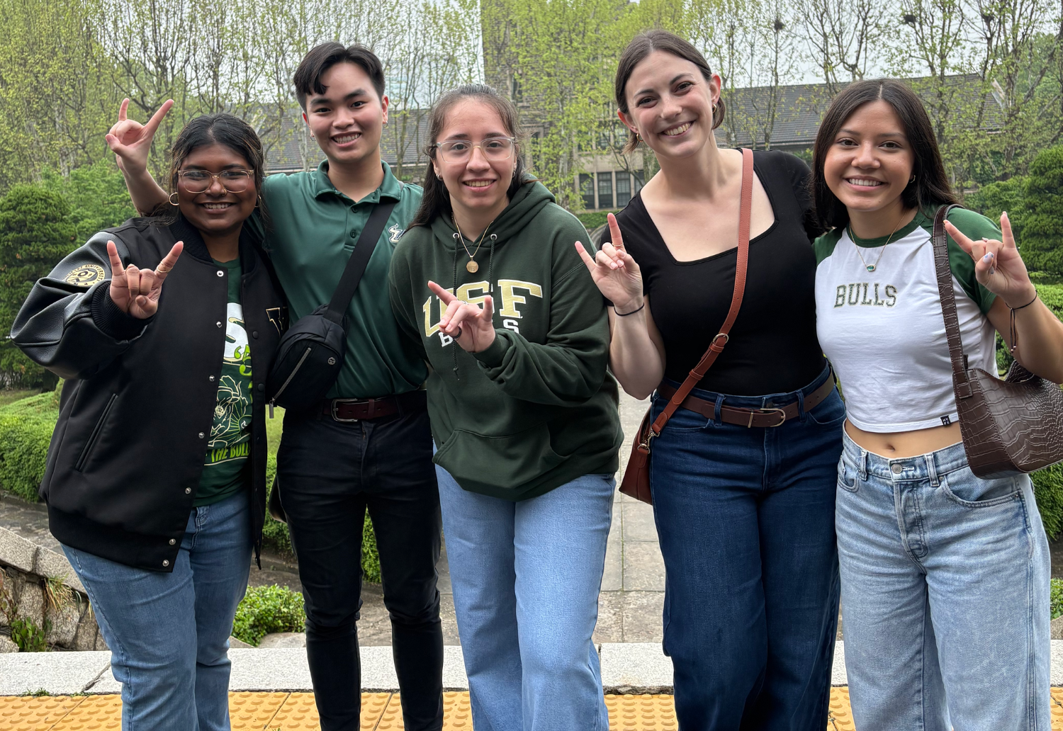 Five people stand at Yonsei University in Seoul holding up the "go bulls" hand sign