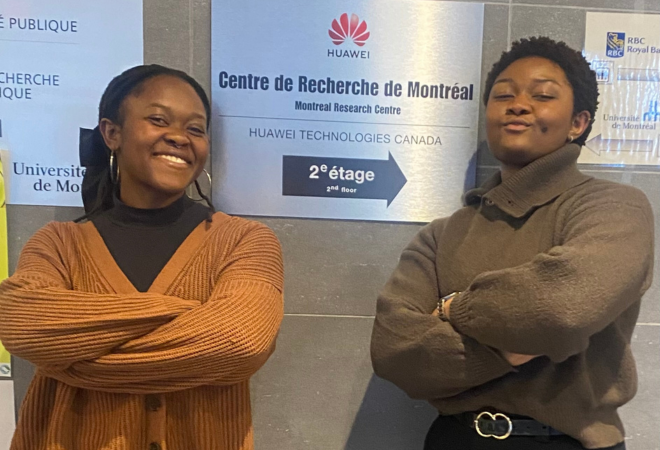 Two women pose with their arms crossed in from of a sign pointing to the Montreal Research Center