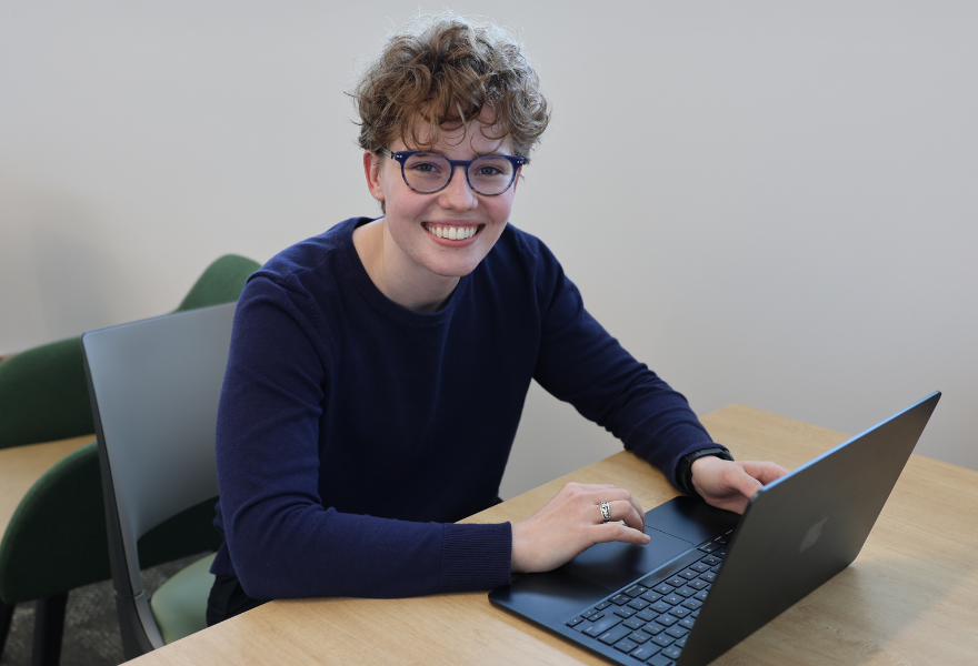 Gray sitting at desk on computer smiling at camera