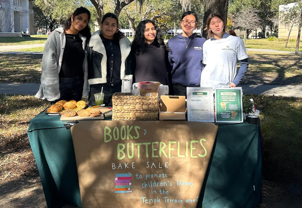 Five women stand behind bake sale table raising money