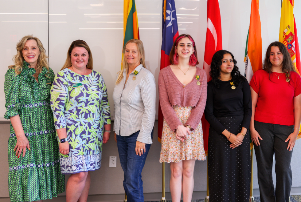 Kiki Caruson, Lauren Chambers, Elisabeth Parker, May Spinney, Afreen Khan, and Lizt Pena stand in front of their Fulbright country's flags in the Judy Genshaft Honors College.