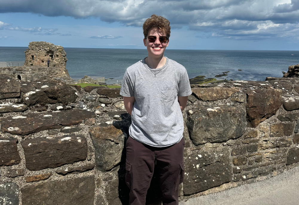Gray stands in front of a stone wall on the coast of Scotland