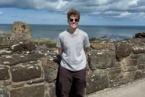 Gray stands in front of a stone wall on the coast of Scotland
