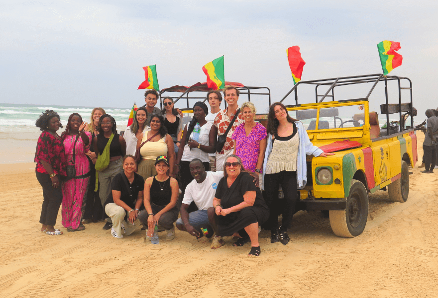 Nico and a group in front of two yellow vehicles with the Senegal flag on top, on the beach 
