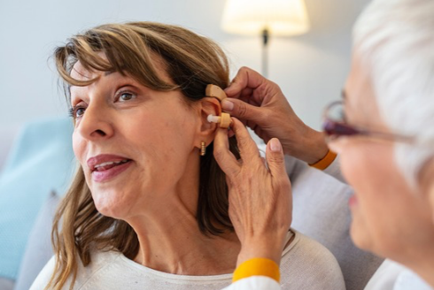 Healthcare professional fits a hearing aid behind a patient's ear during a hearing assessment.