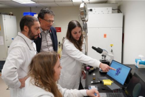 students and faculty in lab coats pointing at a computer featuring their research