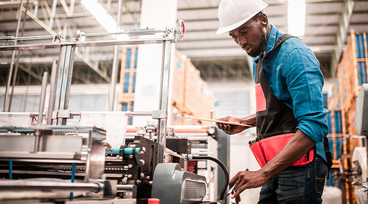 Black male college student in an industrial warehouse at his co-op job programming equipment