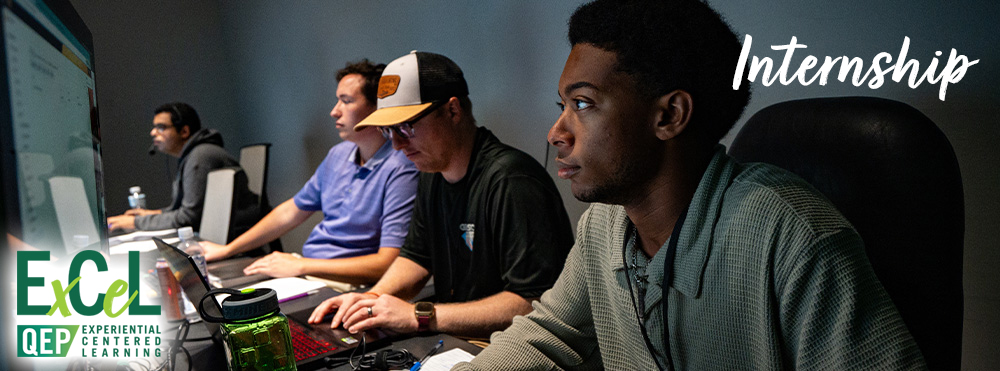 male student television broadcasting intern working on computer in room with professional employees