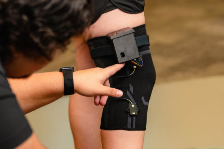 A researcher pointing to a technologically equipped knee brace 