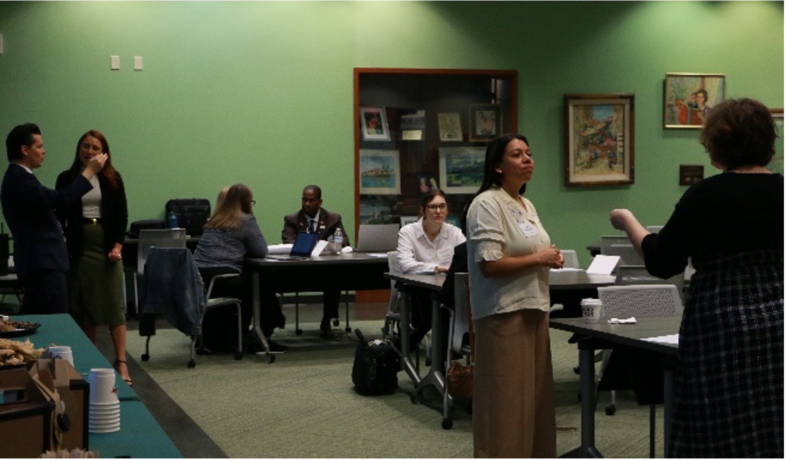 An interior shot of a group of individuals having discussions, some are seated at desks while others stand 