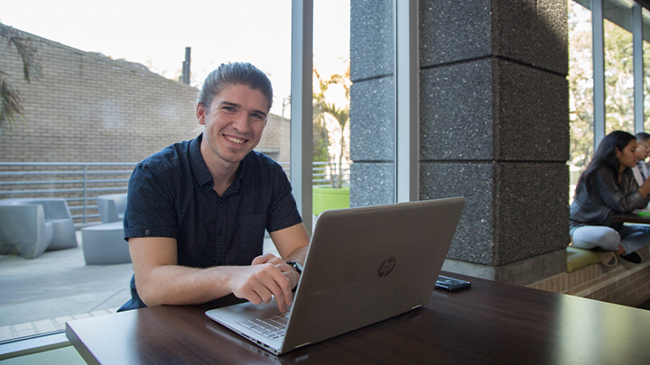 student Brandon working on laptop at a table in Muma College of Business atrium