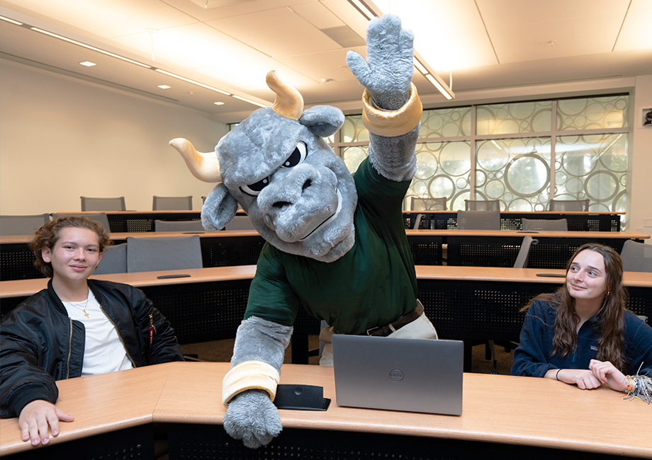 Rocky the Bull raising his hand in the air, in between two students