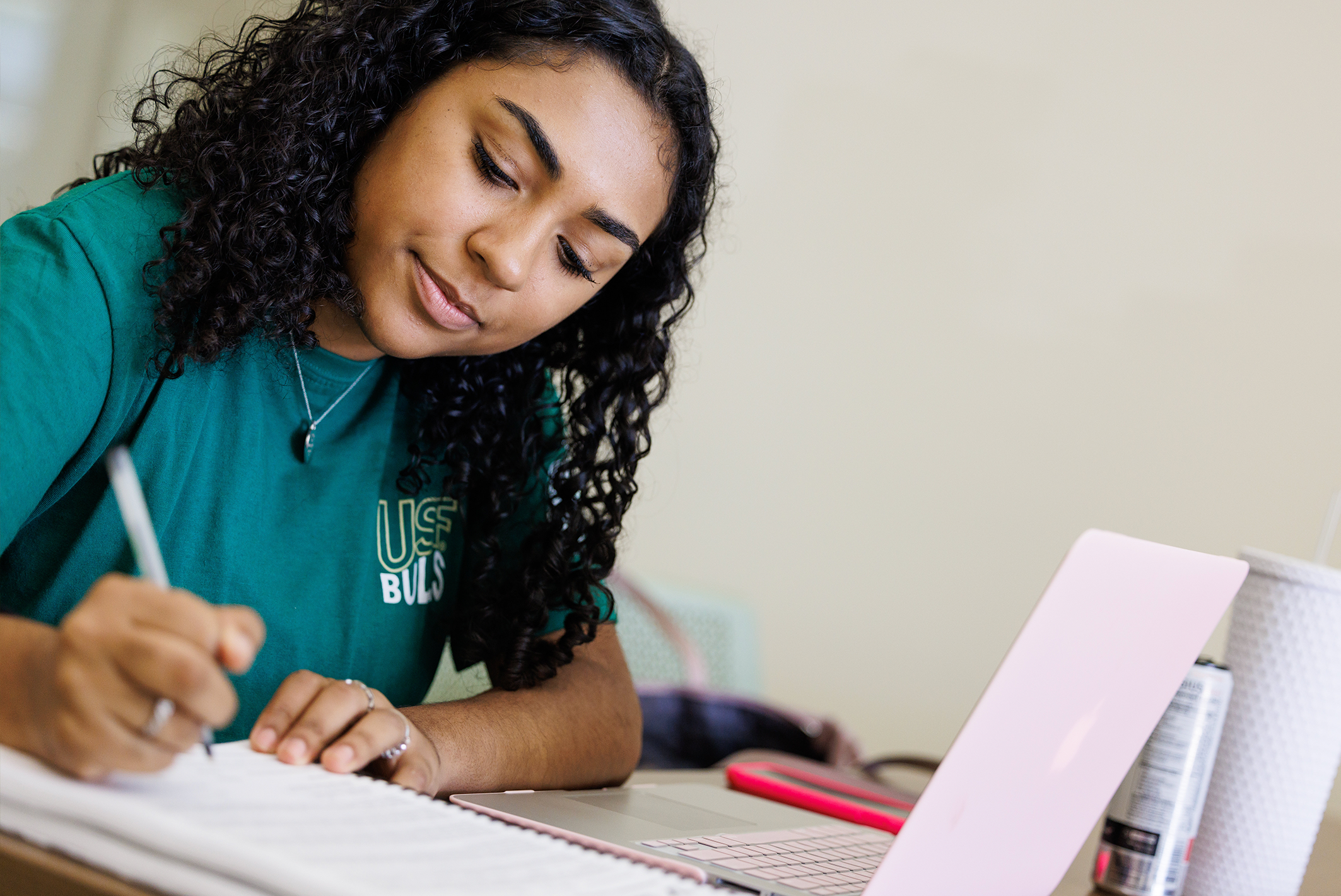 Student studying at a desk, writing notes and using a laptop