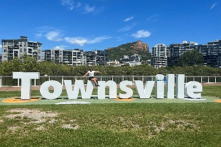 Large white townsville sign with person sitting astride the "w" with the city buildings in the background