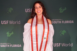 USF graduating student Hawi, posing for a photo with a USF green background. She is wearing a red and white sash representing Lebanon.