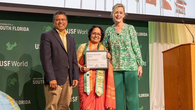 The USF Tampa Provost, Aruna, holding a certificate, and USF World Vice President smile together on stage