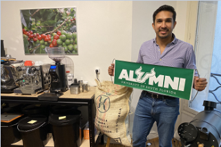 USF global alumnus, Hernan Herrera poses with an alumni sign amongst his coffee import and roasting business