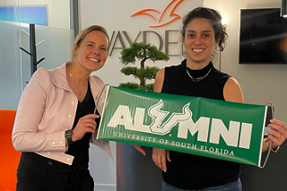 USF global alumnus Alexandre Garnier poses with Vanessa Martinez and an alumni sign during a visit to her Wayden office in Paris.  