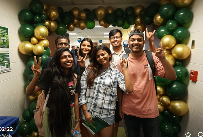 new incoming international students pose for a picture under a green and gold baloon arch