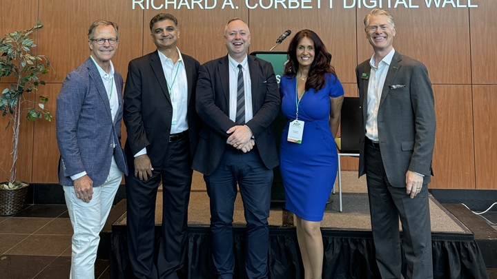 University of South Florida, University of East London, and Tampa Bay business people pose for a picture at the Academia Meets Practice conference - four older caucasian gentleman flank a middle-aged caucasian women in business professional dress