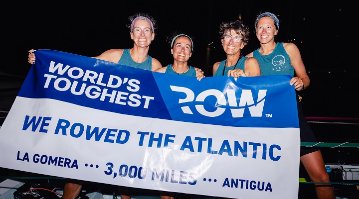 USF team, Salty Science, standing abroad their ship holding a banner proclaiming their successful finish of the World’s Toughest Row-Atlantic race