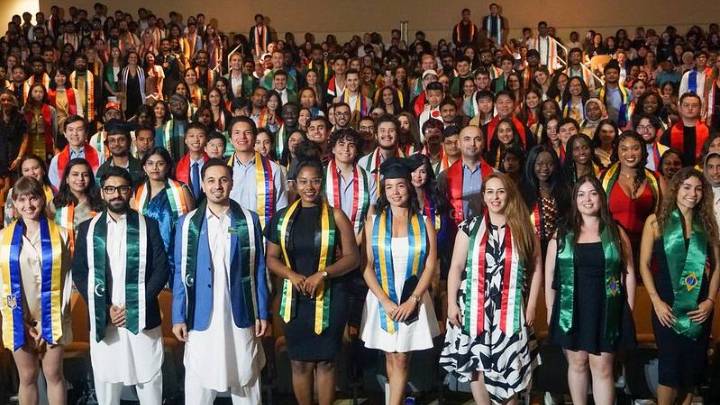 group photograph of USF international students stading as a group at their seats with their country sashes in the MSC Oval Theater auditorium