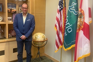 a glasses-wearing Dr. Humberto Gomez from UniNorte in Colombia stading next to a globe of the world in a blue suit