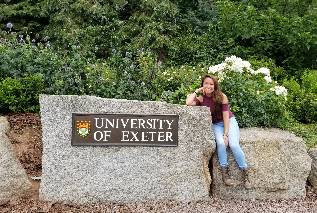 student sitting next to the University of Exeter welcome sign