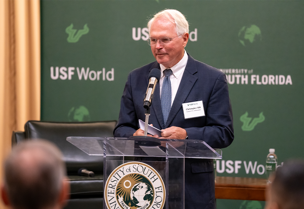 Ambassaor Christopher Hill speaking at the podium with USF logo
