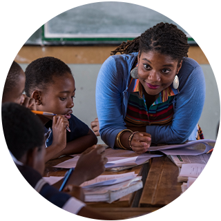 Person leaning over desk where children are sitting