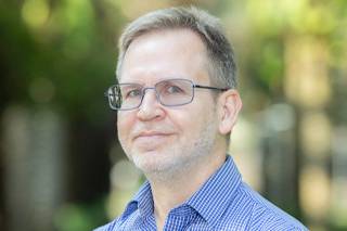 headshot of a caucasian man with short sandy colored hair and glasses wearing a blue checkered shirt