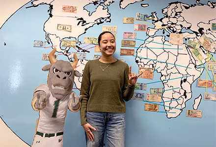 female Colomb ian student at USF posing in front a map of the world with international currencies taped by their respective countries