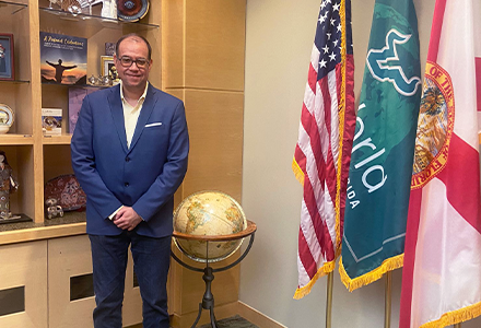 a glasses-wearing Dr. Humberto Gomez from UniNorte in Colombia stading next to a globe of the world in a blue suit