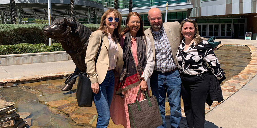 2 female world languages professors from UniNorte in Colombia and USF pose in front of the iconic USF bull with a male and female representative from USF World