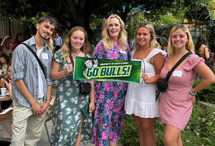 Dr. Kiki posing with alumni and holding a green banner that reads "Go Bulls"