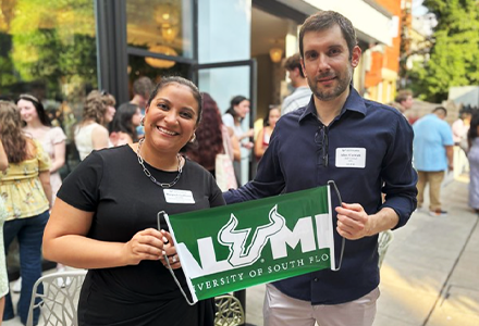Proud alums Raquel Collazzo and Alex Carratt hold green banner that says "Alumni"
