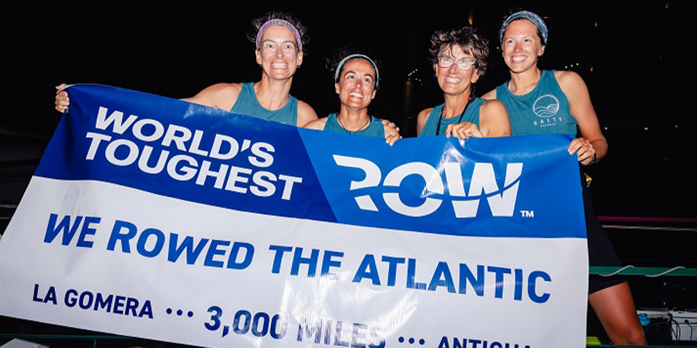 USF team, Salty Science, standing abroad their ship holding a banner proclaiming their successful finish of the World’s Toughest Row-Atlantic race