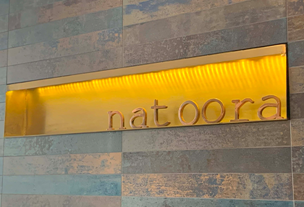 A gold lit sign with the name "natoora"