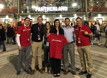 A group of people wearing pantherland shirts in front of a stadium with a lit sign that says "Pantherland"