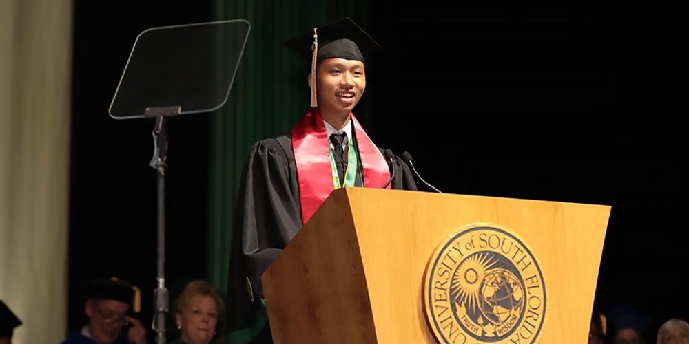 Vietnamese student, Kha Do stands at a podium on stage in regalia while giving a commencement speech
