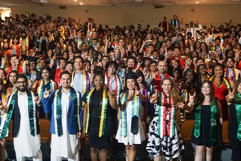 Hundreds of international USF graduation students smiling and doing the bull sign with fingers at camera