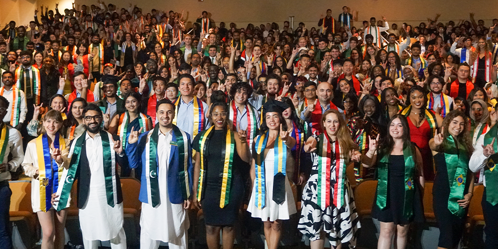 Hundreds of international USF graduation students smiling and doing the bull sign with fingers at camera