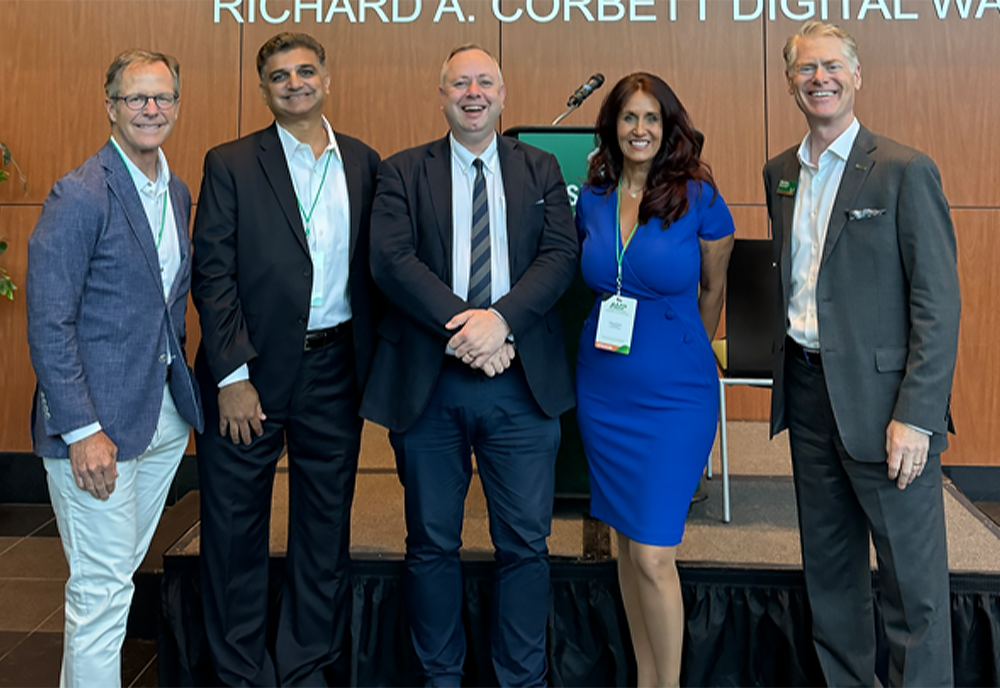 University of South Florida, University of East London, and Tampa Bay business people pose for a picture at the Academia Meets Practice conference - four older caucasian gentleman flank a middle-aged caucasian women in business professional dress