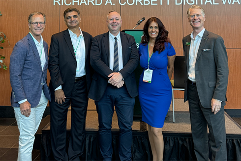University of South Florida, University of East London, and Tampa Bay business people pose for a picture at the Academia Meets Practice conference - four older caucasian gentleman flank a middle-aged caucasian women in business professional dress