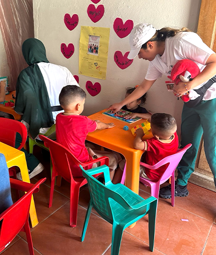 nursing student leaning over table by three children in a classroom setting