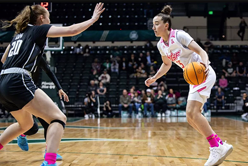 Action shot of USF women's basketball player, Carla Brito, dribbling past an opposing player during a game