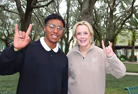 male college student in navy sweater posing next to the middle-aged female VP of USF World