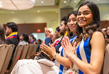 Two students smiling with blue and white sashes on