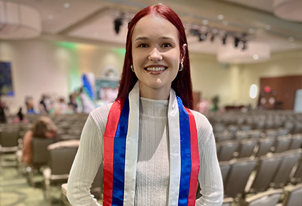A graduating student with red, blue, and white striped sash